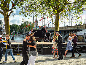 Quatre couples de danseurs effectuent un tango au son de deux musiciens. - Irudia handitu (modu-leihoa)